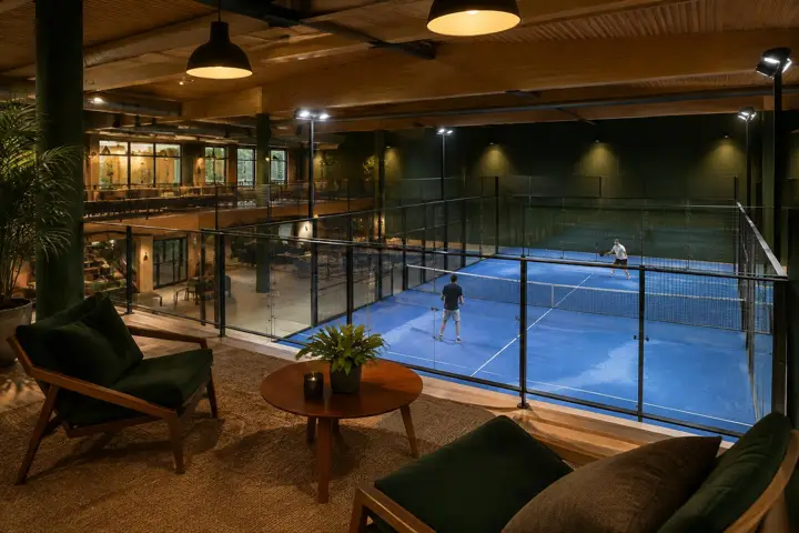 Indoor padel court seen from a clubhouse lounge, showing the relationship between playing space and social areas
